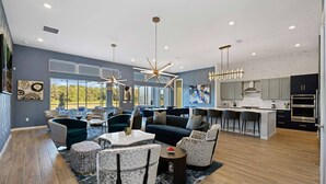 A modern living room with a large window, a kitchen with dark cabinets, and a dining area with a bar.