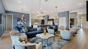 A modern living room with a sofa, chairs, and a coffee table. There is a kitchen in the background with cabinets and a dining area.