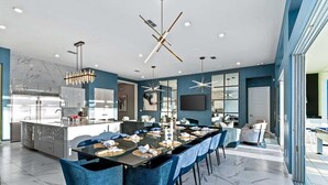 A modern kitchen with a central island, a dining area with blue upholstered chairs, and a large window providing natural light.