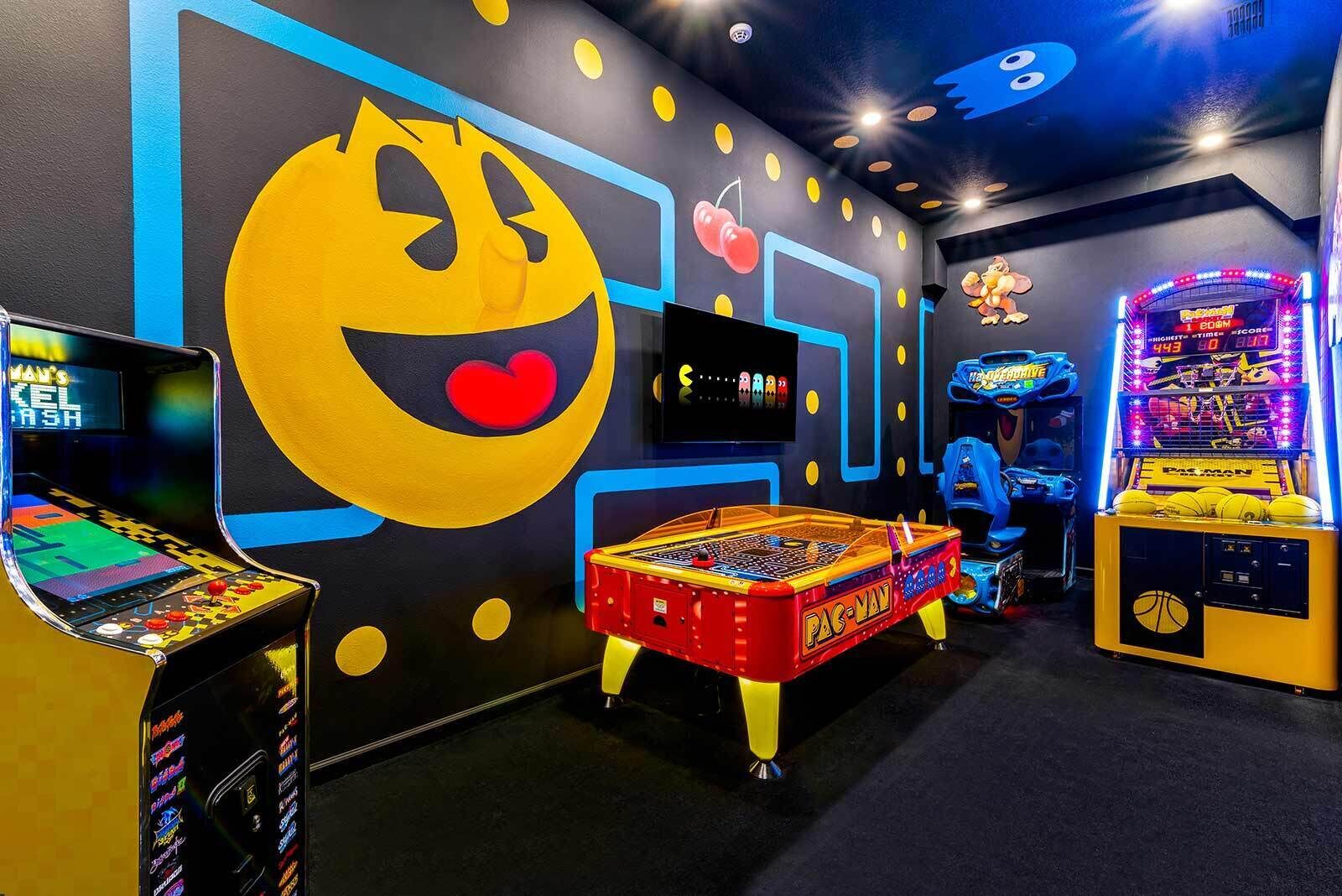 A room with Pac-Man arcade games, a large Pac-Man mural, and a Pac-Man themed table.