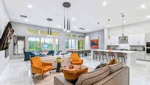 A modern living room with a sofa, chairs, and a dining area with a kitchen in the background. - Fun Home w Mini Playhouse Theme BR, Arcade, Huge Theater, Game Loft, Near Parks (Davenport)