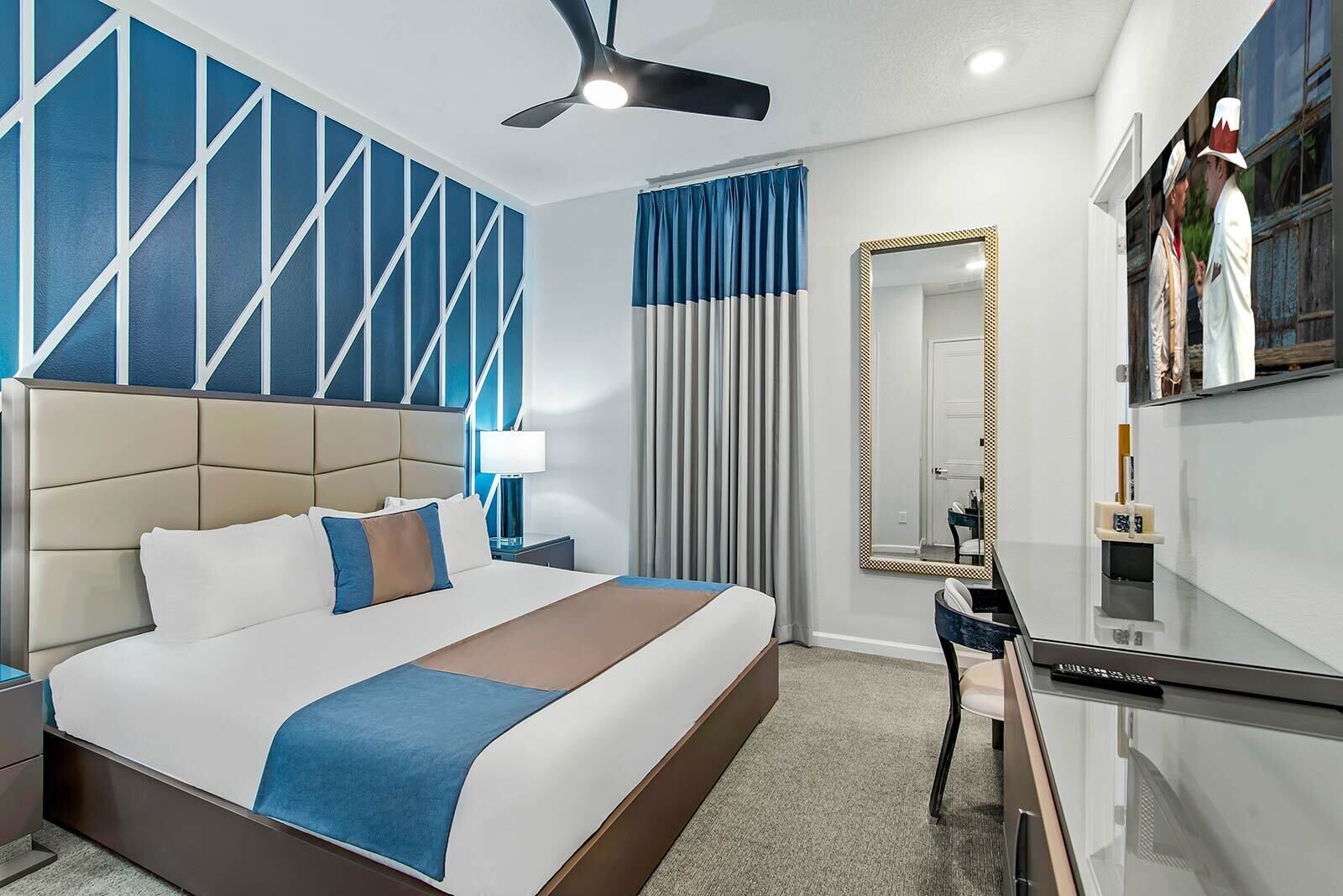 Een moderne hotelkamer met een groot bed, een bureau, een spiegel en een plafondventilator.