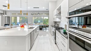 A modern kitchen with a large island, stainless steel appliances, and pendant lighting. - Fun Home w Mini Playhouse Theme BR, Arcade, Huge Theater, Game Loft, Near Parks (Davenport)