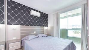 A bedroom with a bed, bedside tables, a wall-mounted air conditioner, and a large window with curtains.