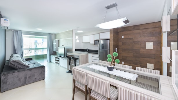 A modern living room with a sofa, dining table, and chairs. There is a kitchen area with a refrigerator, microwave, and cabinets.