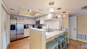A modern kitchen with stainless steel appliances, a central island with bar stools, and pendant lighting. - Beautifully Updated One Bedroom Villa Great for a Couples Getaway! (Hilton Head)