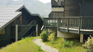 A building with a sloped roof and a wooden deck, surrounded by a grassy area and a gravel path. - 200m from ski slopes, balcony, parking, tv, ski locker, 25m², La Joue du Loup (Agnières-en-Dévoluy)