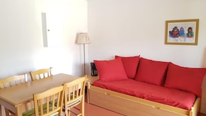 A room with a wooden dining table, four chairs, a red sofa, a lamp, and a framed picture on the wall. - 200m from ski slopes, balcony, parking, tv, ski locker, 25m², La Joue du Loup (Agnières-en-Dévoluy)
