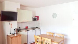 A compact kitchen with white cabinets, a microwave, a kettle, a dishwasher, and a wooden dining table with chairs. - 200m from ski slopes, balcony, parking, tv, ski locker, 25m², La Joue du Loup (Agnières-en-Dévoluy)