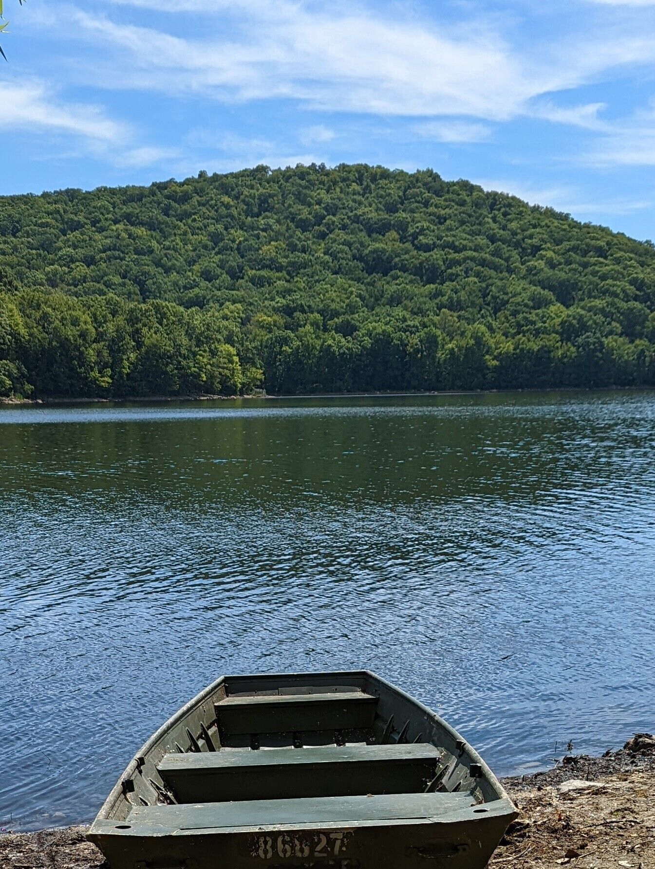 A small boat on a calm lake with a forested hill in the background.
