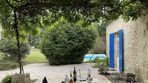 Een terras buiten met een eettafel, omringd door groen en een stenen muur.