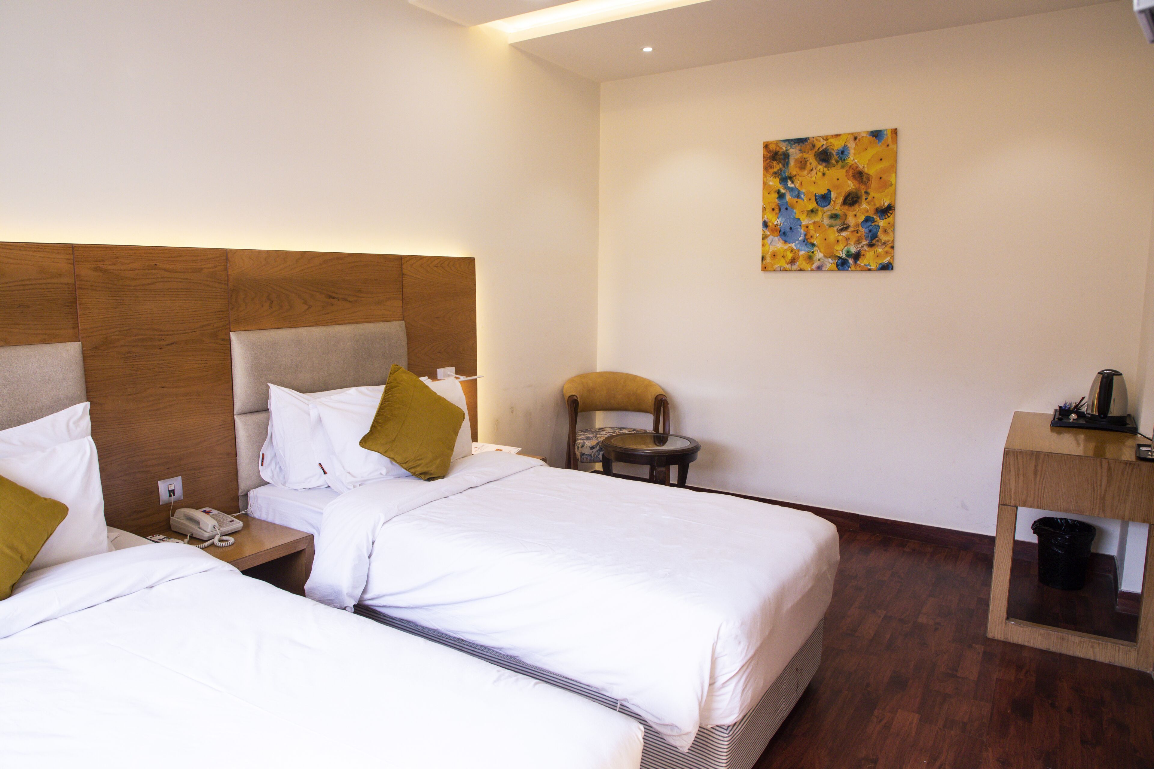 A hotel room with two beds, a wooden headboard, a small table with a chair, and a painting on the wall.
