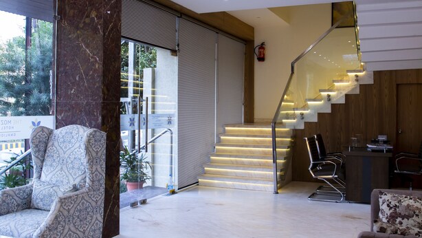 Un interior moderno con suelo de mármol, sillón estampado, escalera con barandilla de vidrio y un candelabro.