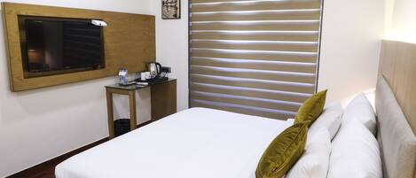 Habitación de hotel con cama, escritorio con cafetera, un cuadro en la pared y ventana con persianas.