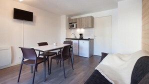 A compact living space with a dining area, kitchenette, and a flat-screen TV mounted on the wall.