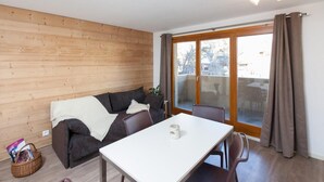 A modern living room with a sofa, a dining table, and a large sliding glass door leading to an outdoor area.