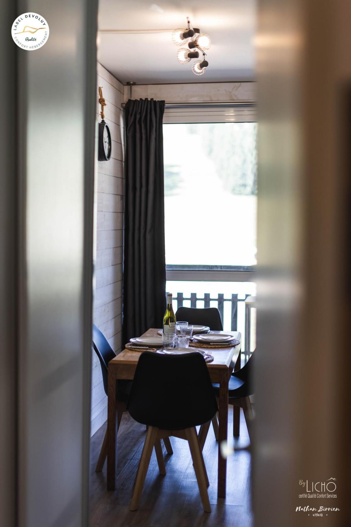 A dining area with a table set for two, a bottle of wine, and a clock on the wall.