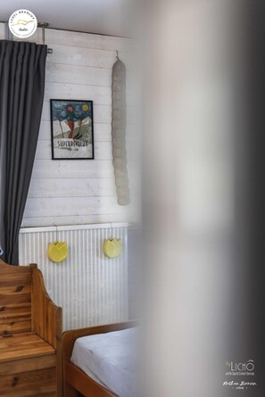 Une chambre à coucher avec un lit en bois, une tête de lit blanche, un tableau représentant un skieur et un radiateur orné de deux décorations en forme de cœur jaune.
