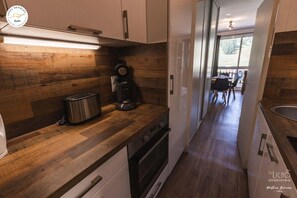 Une cuisine moderne avec des plans de travail en bois, une machine à café et un grille-pain. On aperçoit un coin repas à l’arrière-plan.