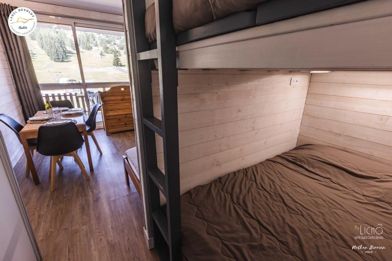 A compact room with a bunk bed, a dining area with a table and chairs, and a window with a view of a forest.