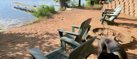 Un cadre idyllique au bord d’un lac, avec des fauteuils Adirondack verts, un chien et une jetée en bois.