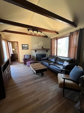 A cozy living room with a fireplace, a sofa, a coffee table, and a wooden floor. - Cozy Log Cabin on Little Spider Lake (Hayward)