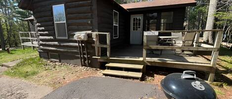 A log cabin with a porch, a grill, and a bench.