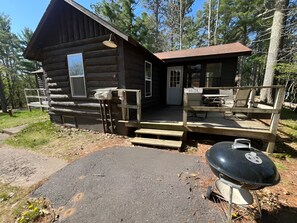A log cabin with a porch, a grill, and a bench.