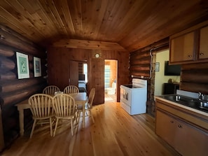 A log cabin interior with a dining area, wooden chairs, a white stove, and a kitchen with cabinets and a sink. - Cozy Log Cabin on Little Spider Lake (Hayward)