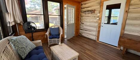 A log cabin interior with a wooden floor, a wicker sofa with blue cushions, a small table, and a door.