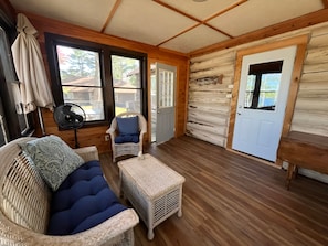 A log cabin interior with a wooden floor, a wicker sofa with blue cushions, a small table, and a door. - Cozy Log Cabin on Little Spider Lake (Hayward)