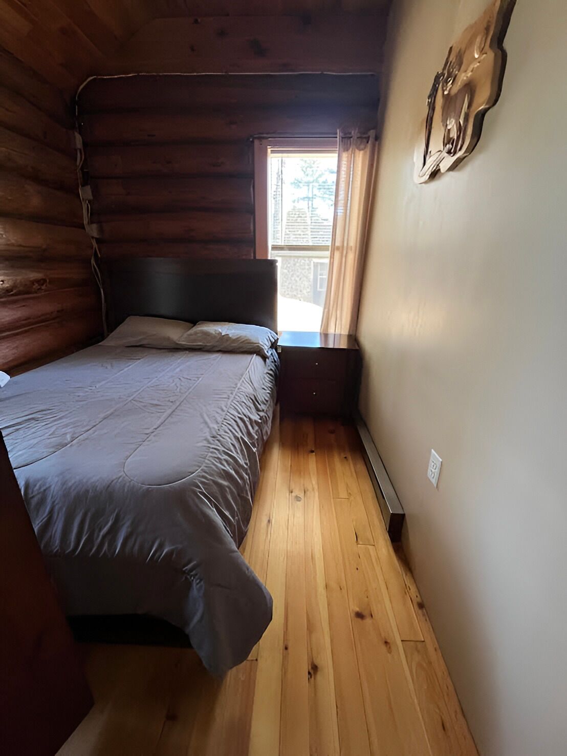 Une pièce de cabane en bois comprenant un lit, une fenêtre et un luminaire fixé au mur.
