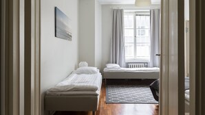 Un couloir étroit avec deux lits simples, un radiateur et une fenêtre avec des rideaux.