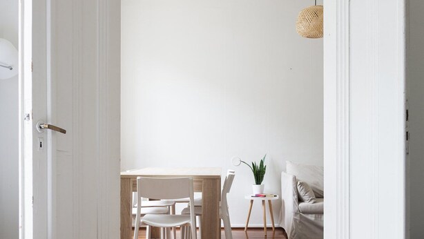 Une pièce comprenant un lit, un plancher en bois, une table à manger avec des chaises, une petite table avec une plante et un luminaire suspendu.