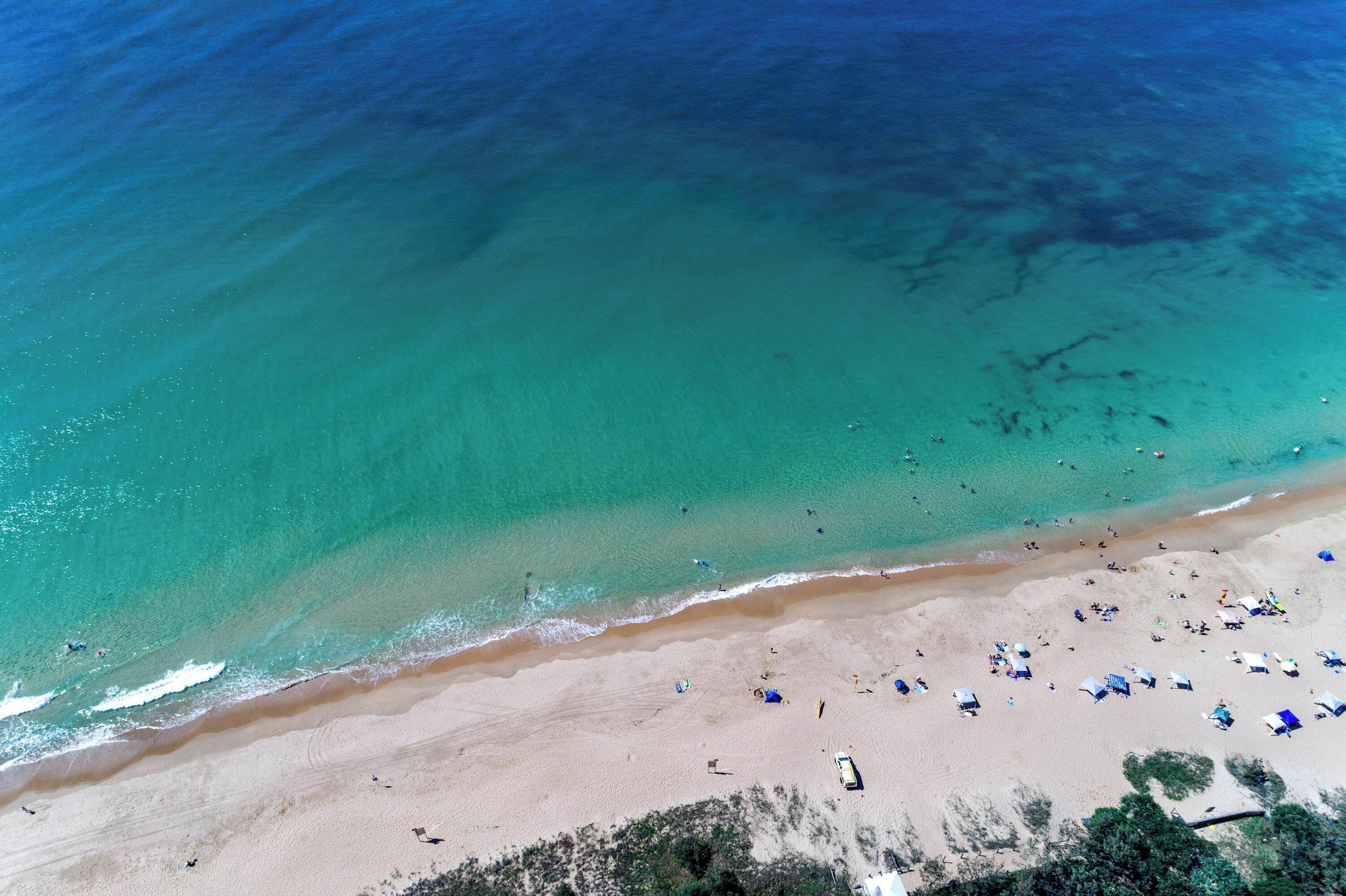 A beach with clear turquoise water, sandy shore, and several tents and umbrellas.