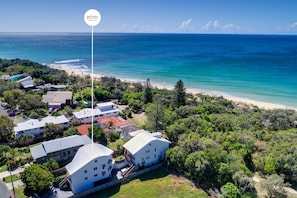 A coastal residential area with multiple buildings, a clear view of the ocean, and a sign indicating a welcome message. - Spacious Seaside Oasis on Dicky Beach (Dicky Beach)