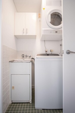 Une petite buanderie équipée d’un lave-linge, d’un sèche-linge et d’un petit meuble de rangement.