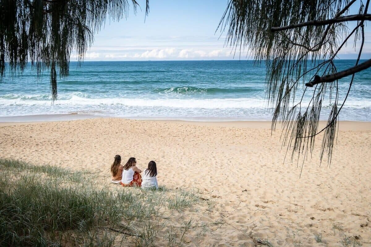 A beach with three people sitting on the sand, overlooking the ocean.
