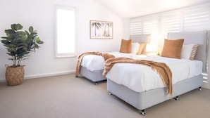 A bedroom with two beds, a potted plant, a framed picture, and a window with blinds.