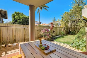 A wooden deck with a table set for a meal, surrounded by a wooden fence and a garden.