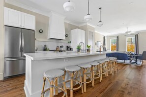 A modern kitchen with a stainless steel refrigerator, white cabinetry, and a bar area with stools.