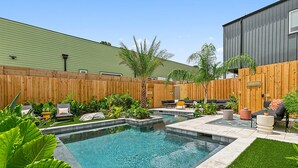 Un jardin avec une piscine, du mobilier d’extérieur et une clôture en bois.