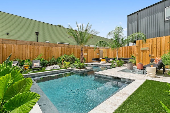 A backyard with a swimming pool, outdoor furniture, and a wooden fence.