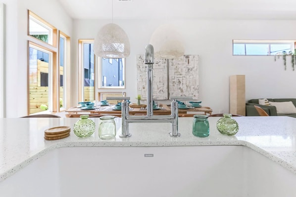 A kitchen with a modern faucet, a white countertop, and a view of the dining area.