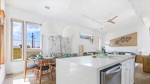 A modern kitchen with a large island, wooden chairs, pendant lights, and a view of the outdoors. - Paradise | Private Hot Tub + Shared Heated Pool (New Orleans)