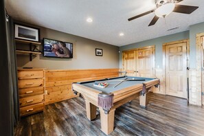 A pool table in a room with wooden cabinets, a ceiling fan, and wooden doors.