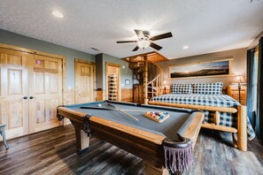 A pool table with a wooden bench, a bed with checkered bedding, and a ceiling fan.