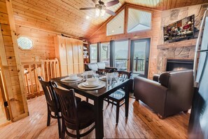 Un interior de madera con una mesa de comedor preparada para cuatro personas, una chimenea y un televisor montado en la pared.