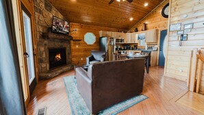 Un interior de cabaña acogedor, con chimenea de piedra, techo de madera y una kitchenette.