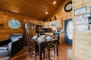 A wooden cabin interior with a dining table set for four, a refrigerator, a microwave, and wooden cabinets.